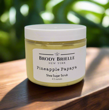 Load image into Gallery viewer, Jar of Pineapple Papaya Shea Sugar Scrub by Brody Brielle on a wooden surface with a blurred green background
