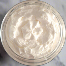 Load image into Gallery viewer, Close-up of a glass container filled with Brody Brielle cocoa + Cashmere Body Butter on a marble table
